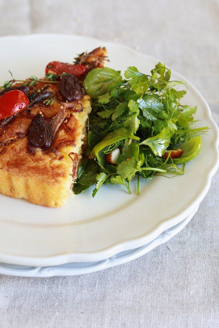 A slice of pissaladière with olives, onions and tomatoes, with a side salad