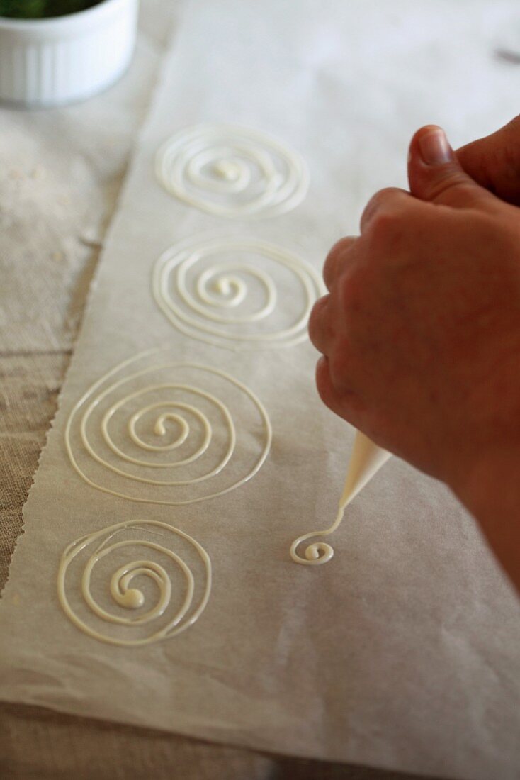 White chocolate spirals being piped onto grease-proof paper