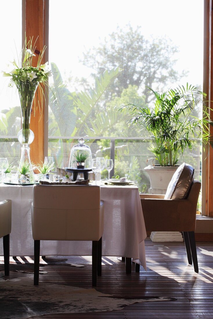 A table laid with vases of flowers and grasses in front of a window with a view of the garden