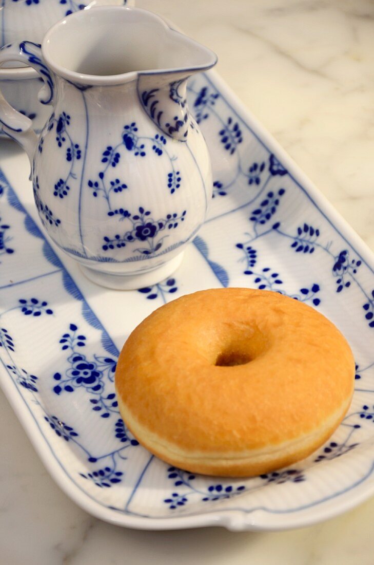 Ein Doughnut und ein Milchkännchen auf einem blau-weissen Teller