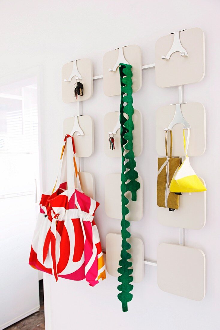 Ladies' accessories and keys hanging on white retro coat rack with shiny metal hooks