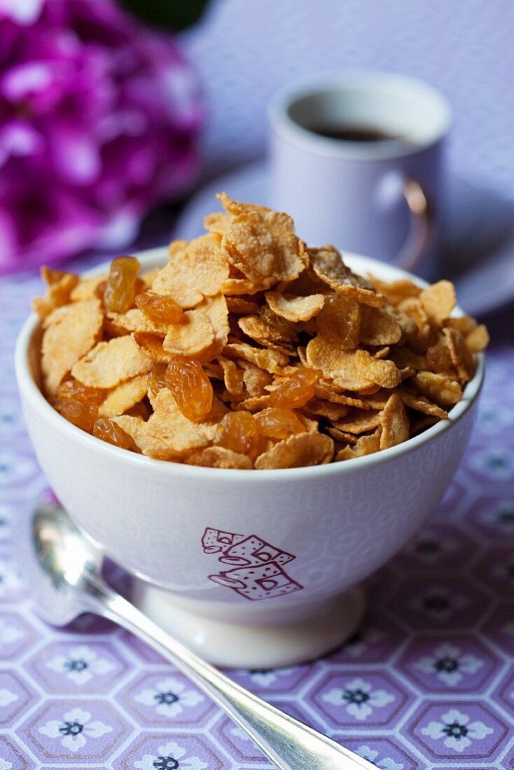 A bowl of cornflakes and raisins on a breakfast table
