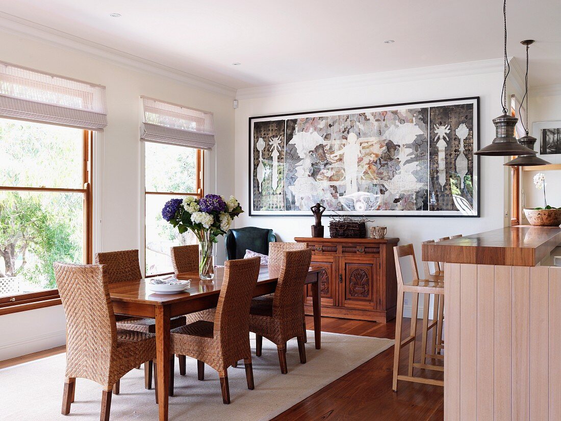 Wicker chairs with tall backrests around classic dining table; wood-clad breakfast bar to one side