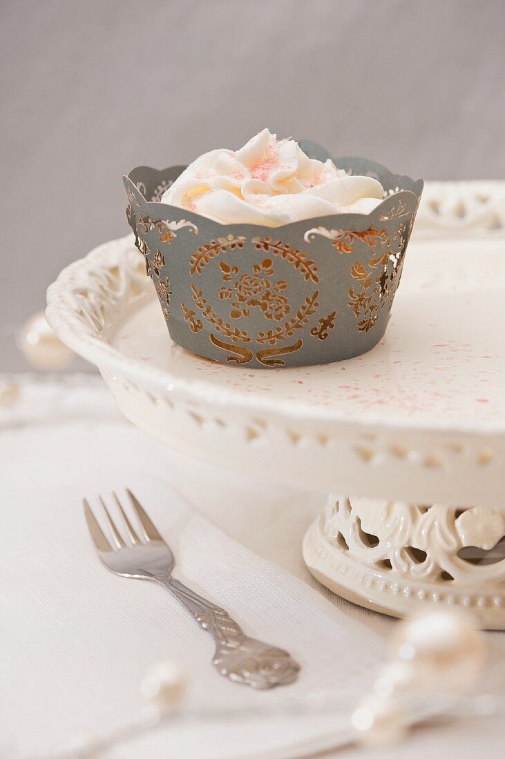 A cupcake with pink frosting on a cake stand