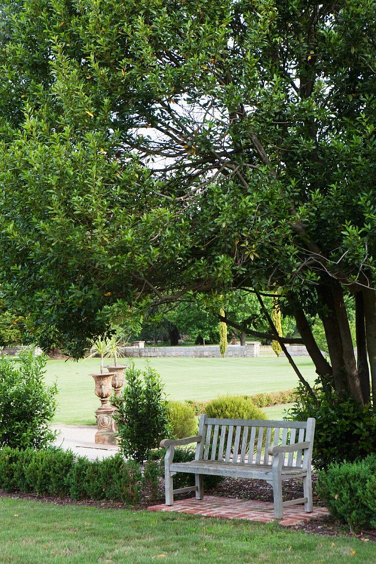 Wooden bench in simply country style framed by a box tree on the romantic grounds of a castle; antique amphoras in the background