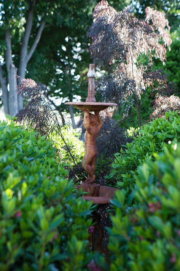 Antike Gartenskulptur zwischen Sträuchern