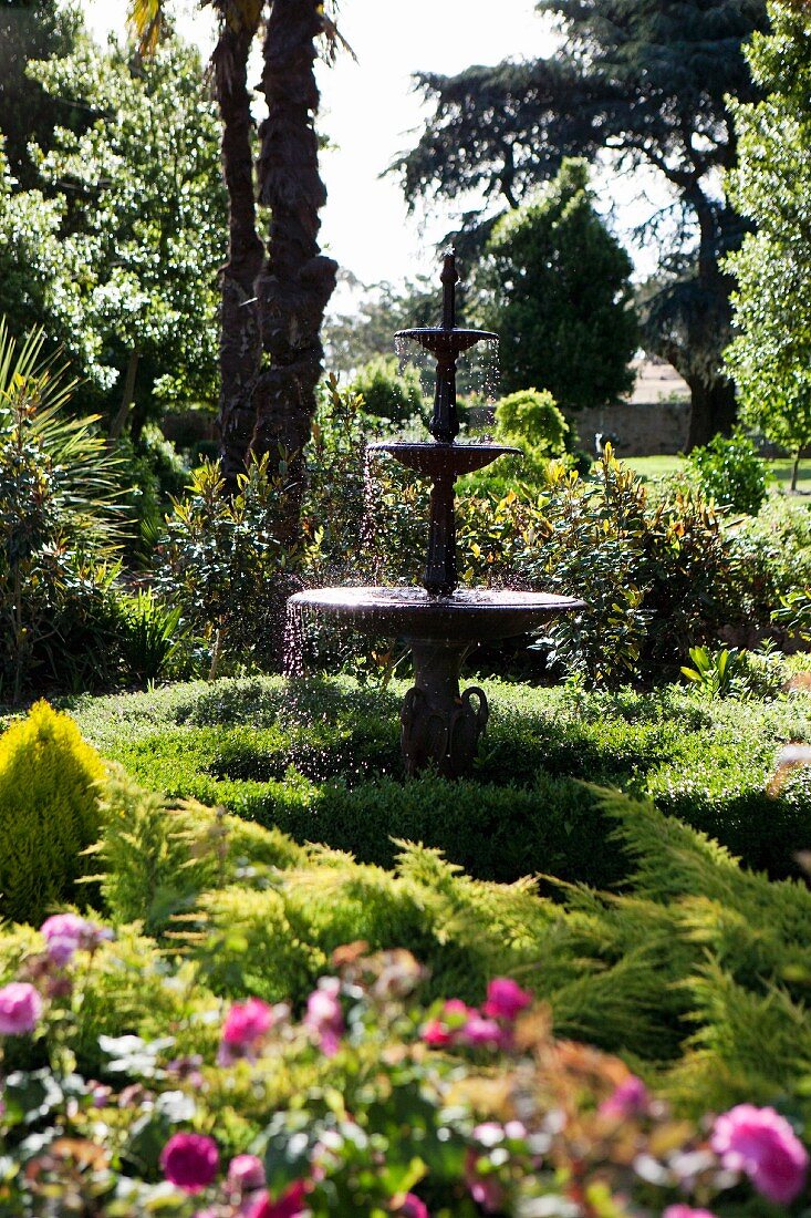 Klassischer, mehrschaliger Springbrunnen zwischen üppigem Grün einer historischen Gartenanlage