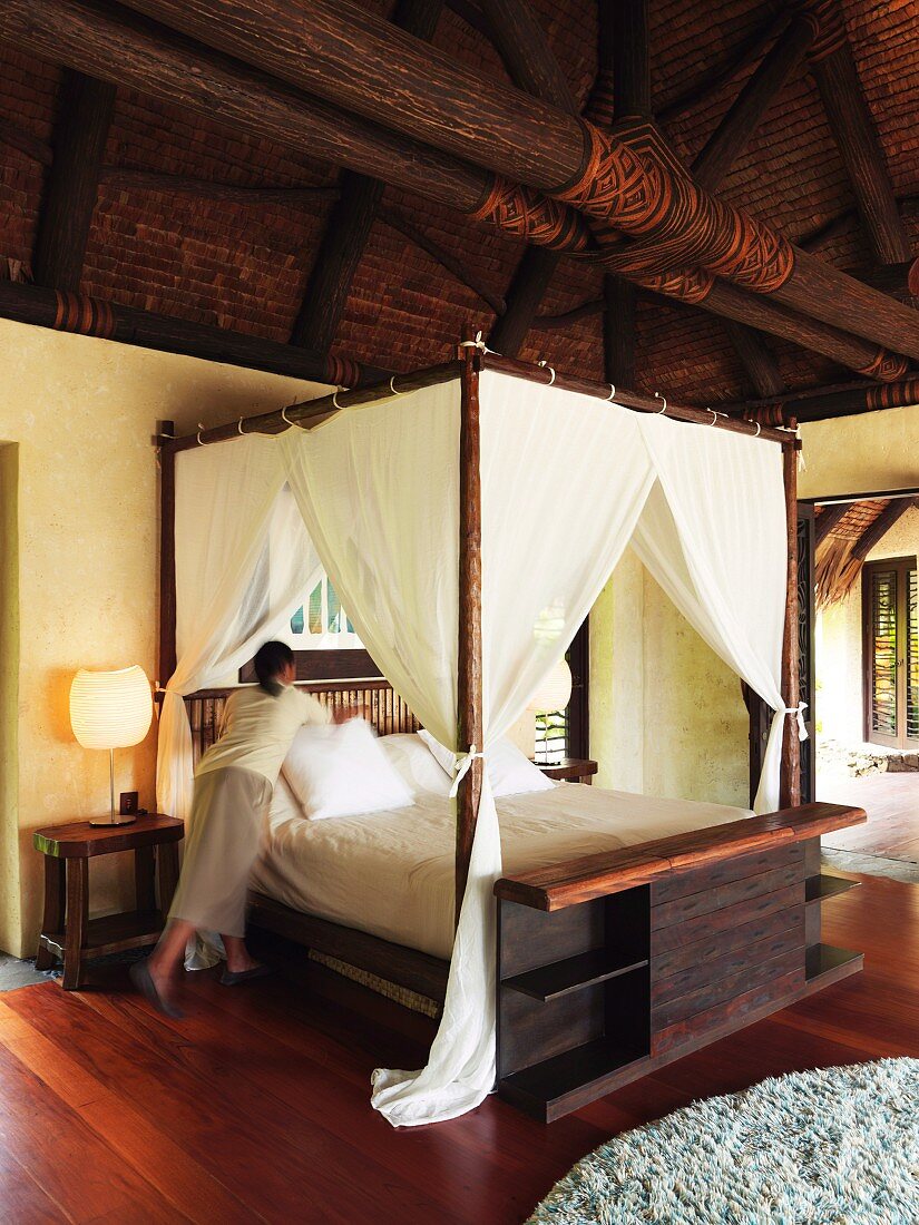 Chambermaid making bed in elegant, Oriental wooden house