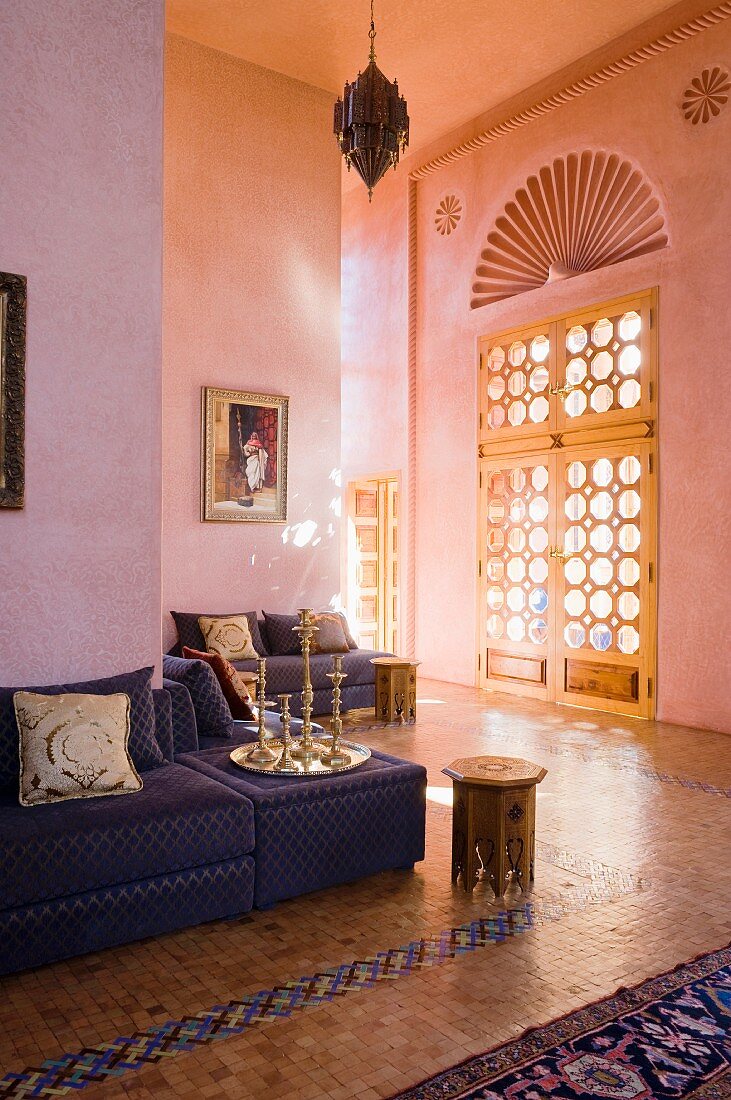 Velvet covered seating around the walls of a salon marocain with tiled floors and octagonal coffee table