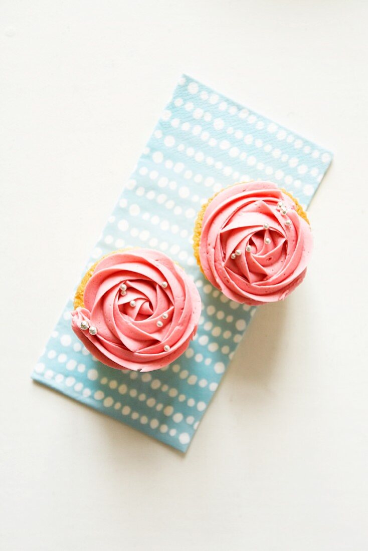 Two cupcakes decorated with strawberry cream and silver balls