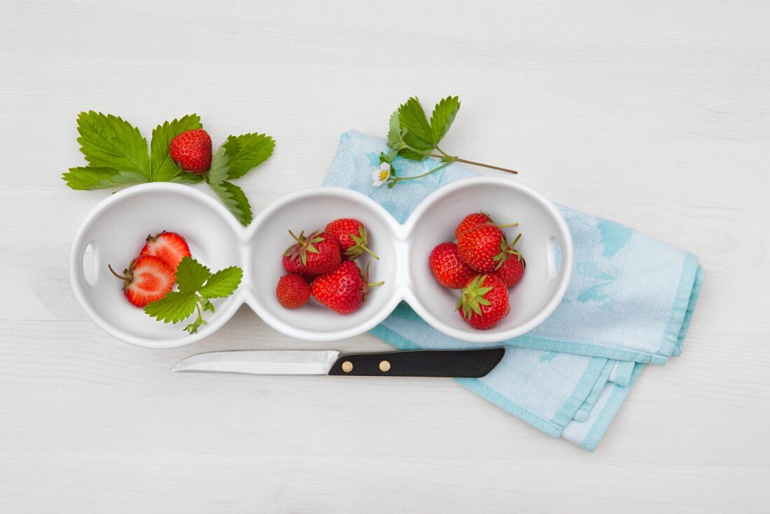 Fresh strawberries with leaves and flowers in bowls