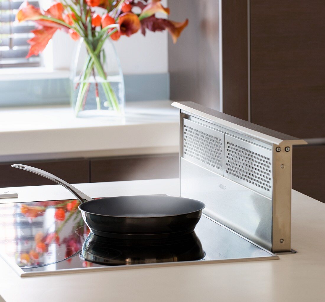 A frying pan on an induction hob with retractable extractor fan