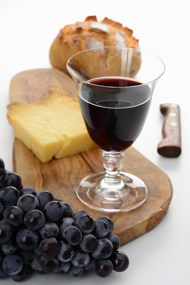A glass of red wine, bread, cheese and grapes