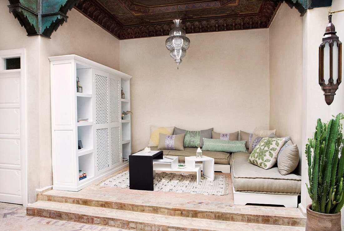 Loggia in orientalischem Stil mit Polstermöbeln und modernem Tischmöbel auf abgestuftem Podest; eine prachtvolle Holzdecke und eine silberfarbene verzierte Pendelleuchte lassen hohe Kunstfertigkeit erkennen