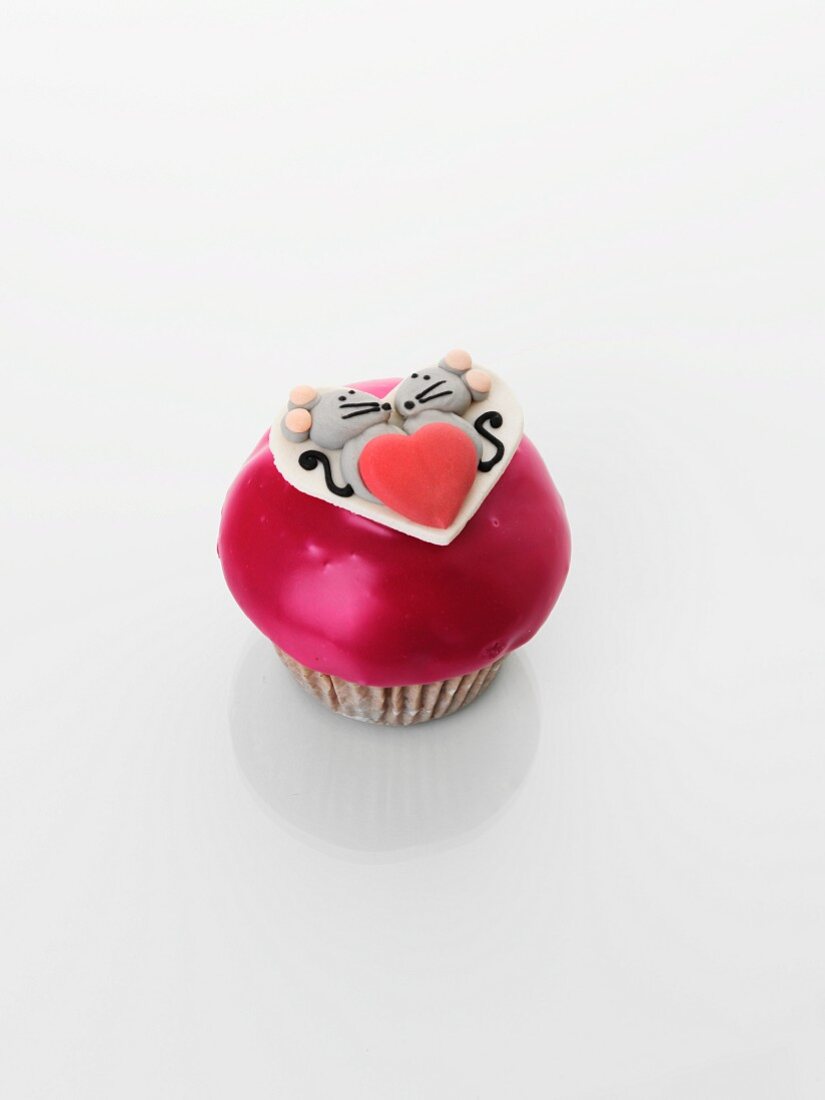 A cupcake decorated with a mouse couple and a heart