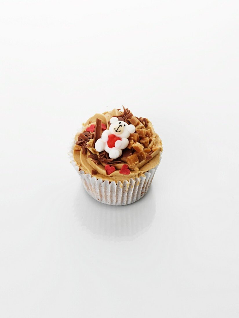 A cupcake decorated with caramel, a teddy bear and hearts