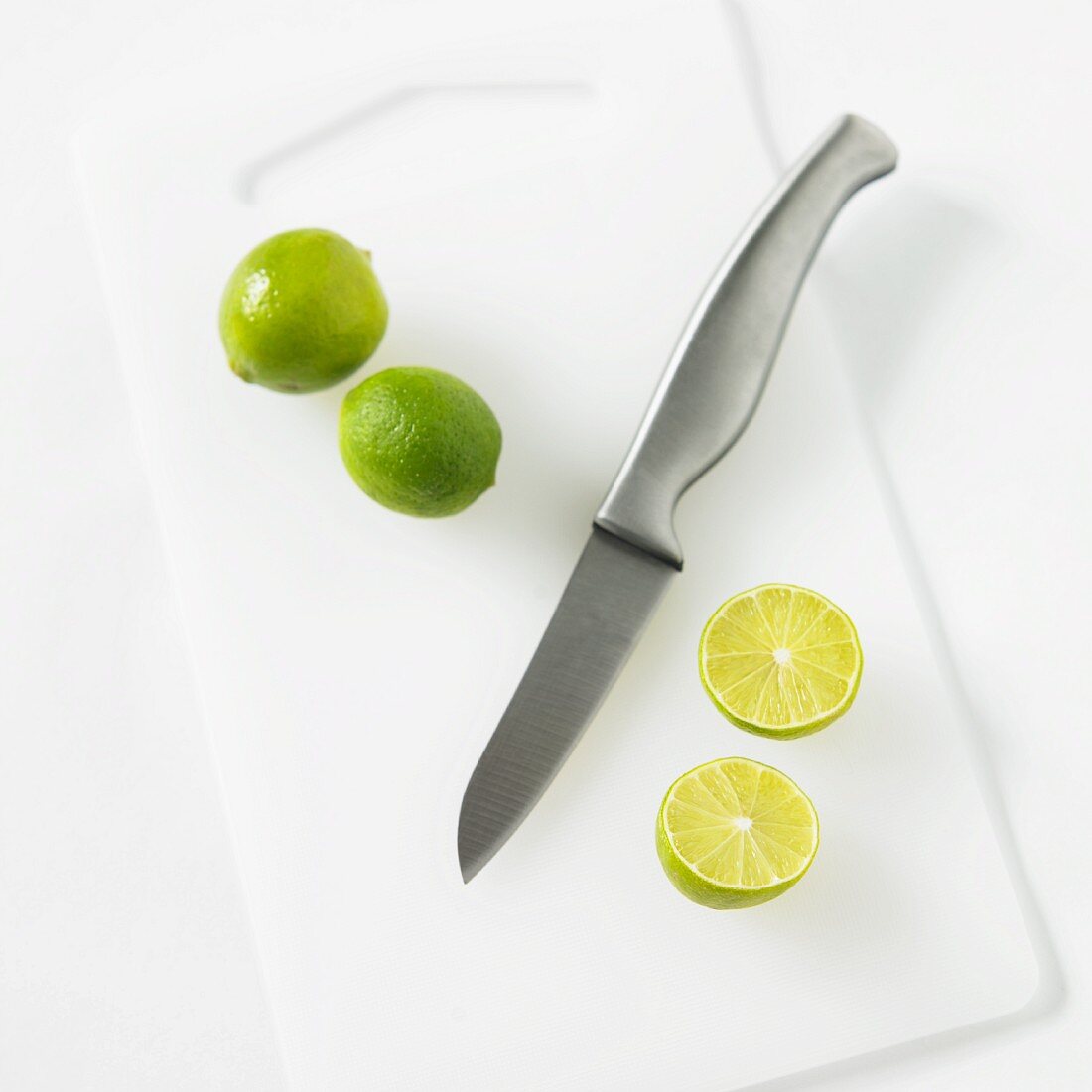 Zwei ganze & eine halbierte Limette mit Messer auf Schneidebrett