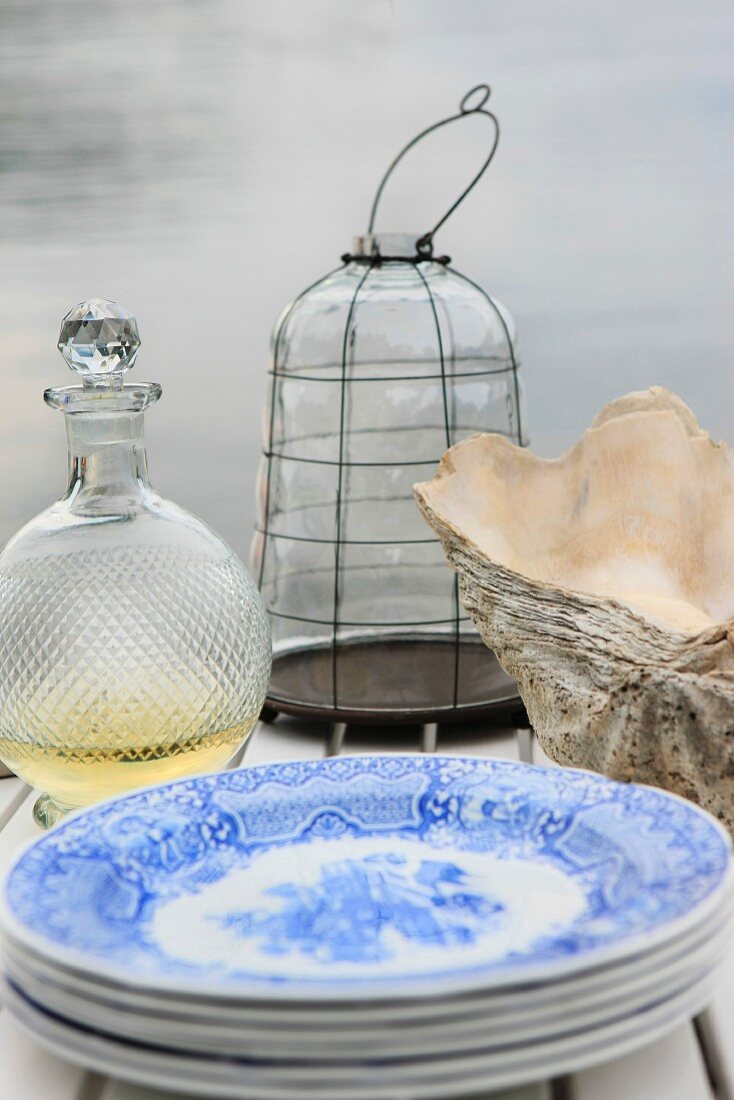 Tellerstapel, Karaffe, Muschelschalen und Windlicht auf einem Holztisch