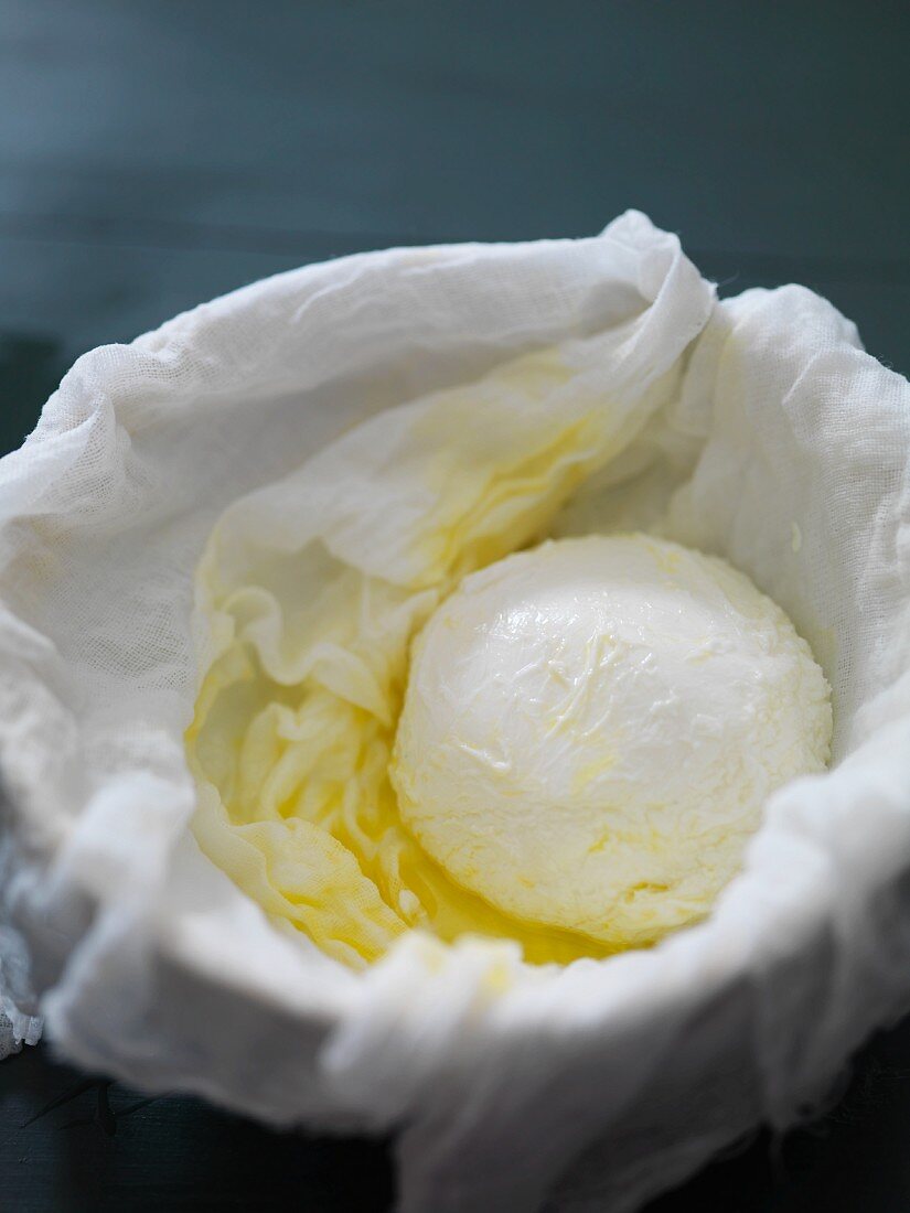 Mozzarella and olive oil in bowl lined with a muslin cloth