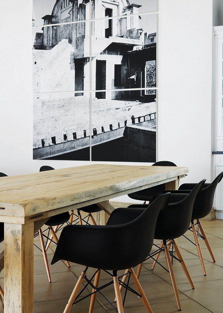 Rustic wooden table and black Eames shell chairs in front of multi-panel photograph on white wall