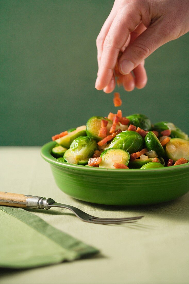 Hand streut Speckwürfel über Rosenkoh