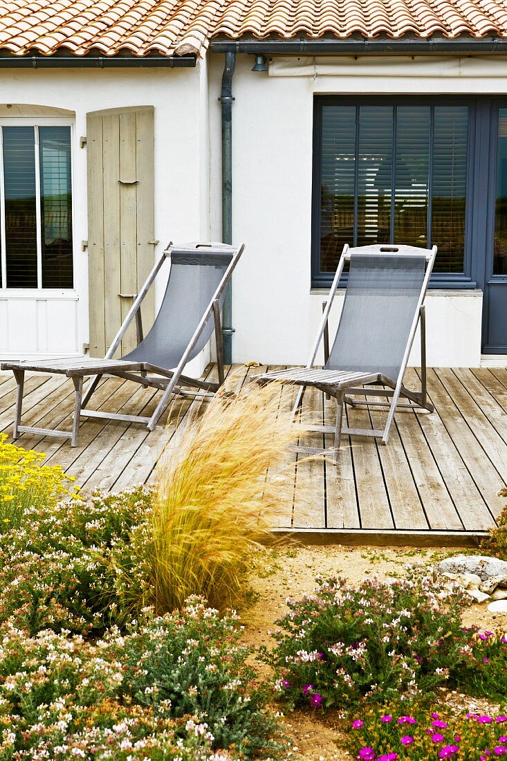 Blooming flowers on a terrace with loungers made of weathered wood at a country home