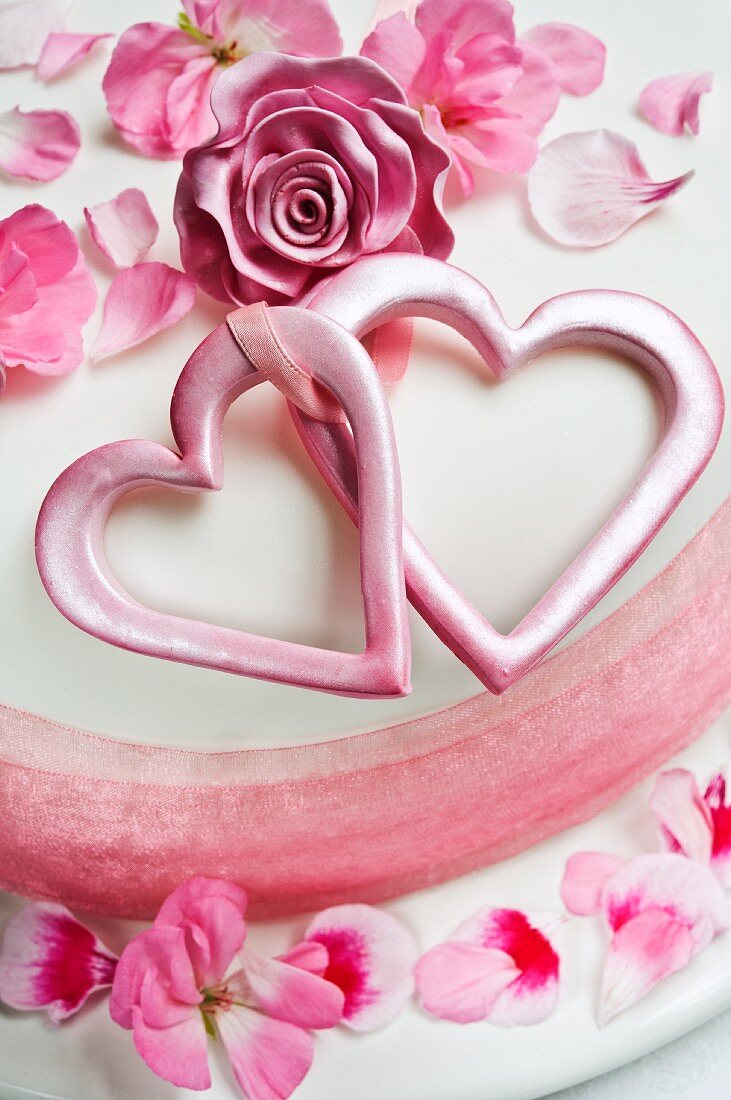 A white cake decorated with hearts, sugar roses and flower petals