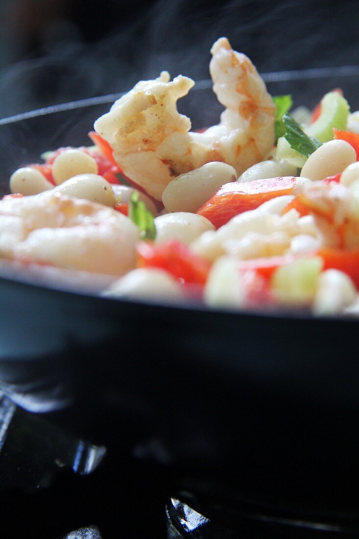 White beans with celery, pepper and prawns in a pan