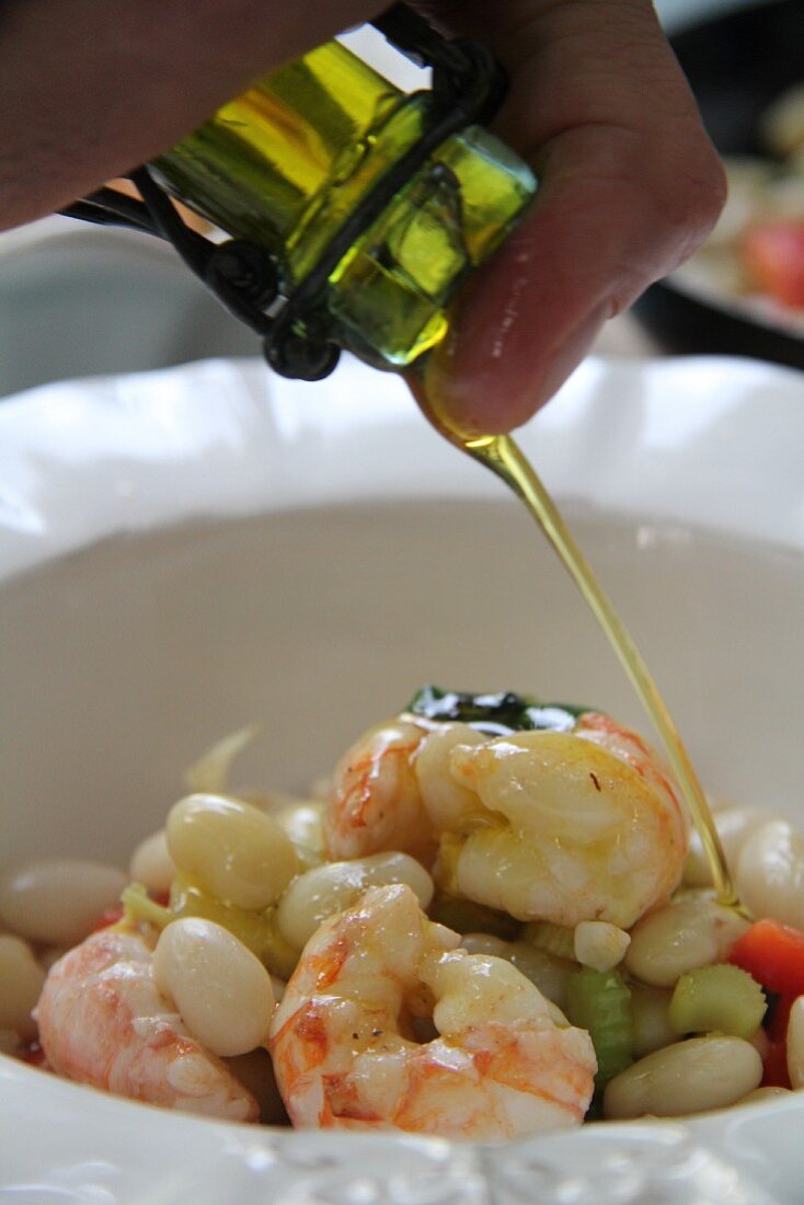 White beans with celery, pepper and prawns being drizzled with olive oil