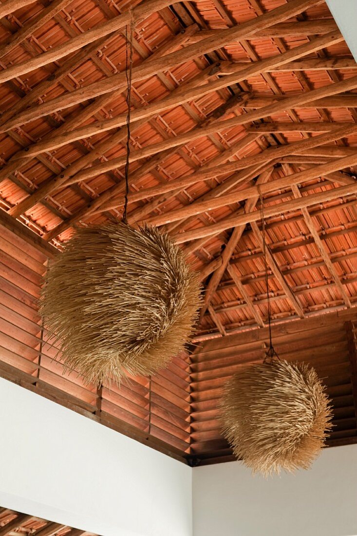 Hohe Dachkonstruktion aus Ebenholz mit an den Holzbalken hängenden Kugellampen aus Naturmaterialien