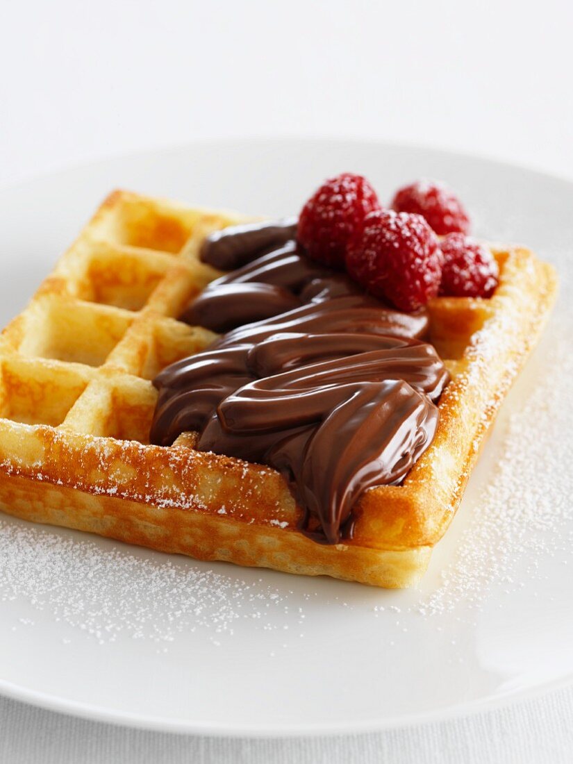A waffle topped with chocolate spread and raspberries