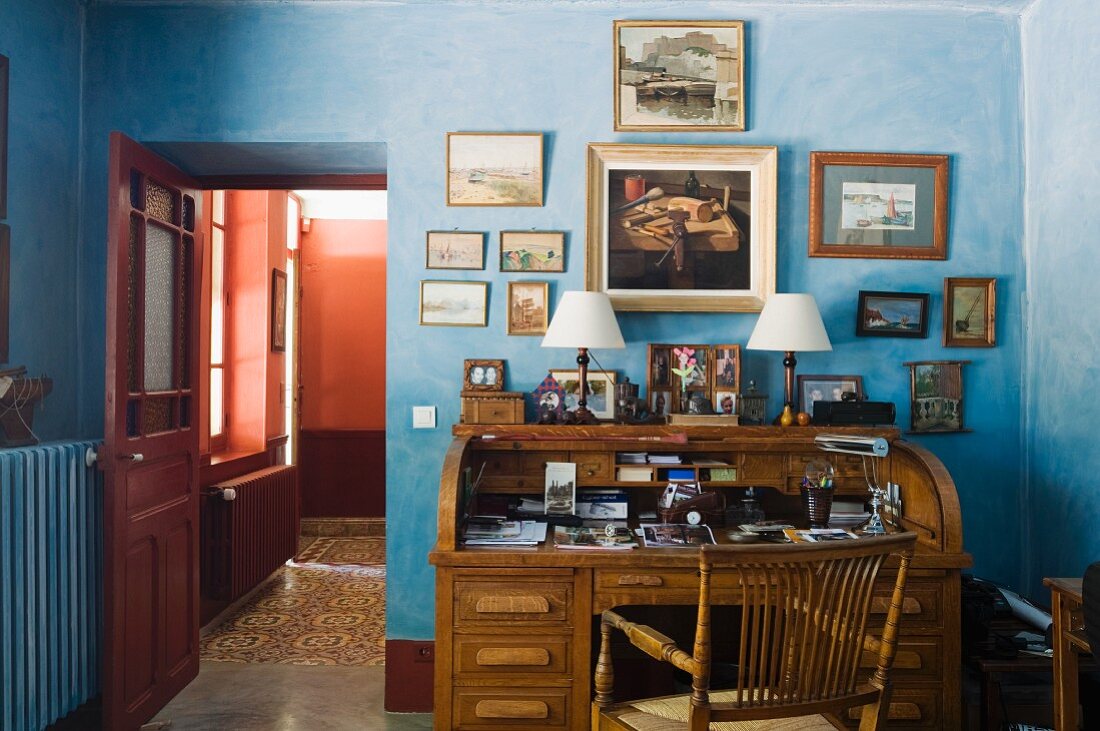 Antiker Schreibtisch mit darüberhängender, kleiner Kunstgemäldesammlung in pastellblauem Arbeitszimmer