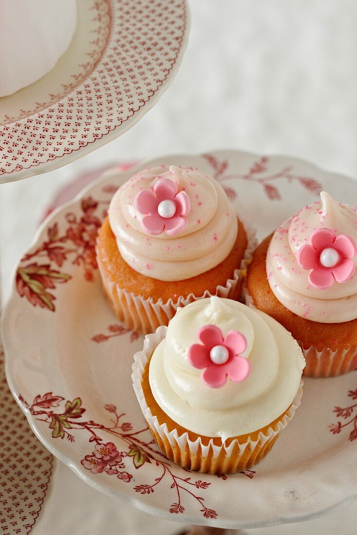 Drei Vanille-Cupcakes mit rosa Zuckerblüten auf Teller