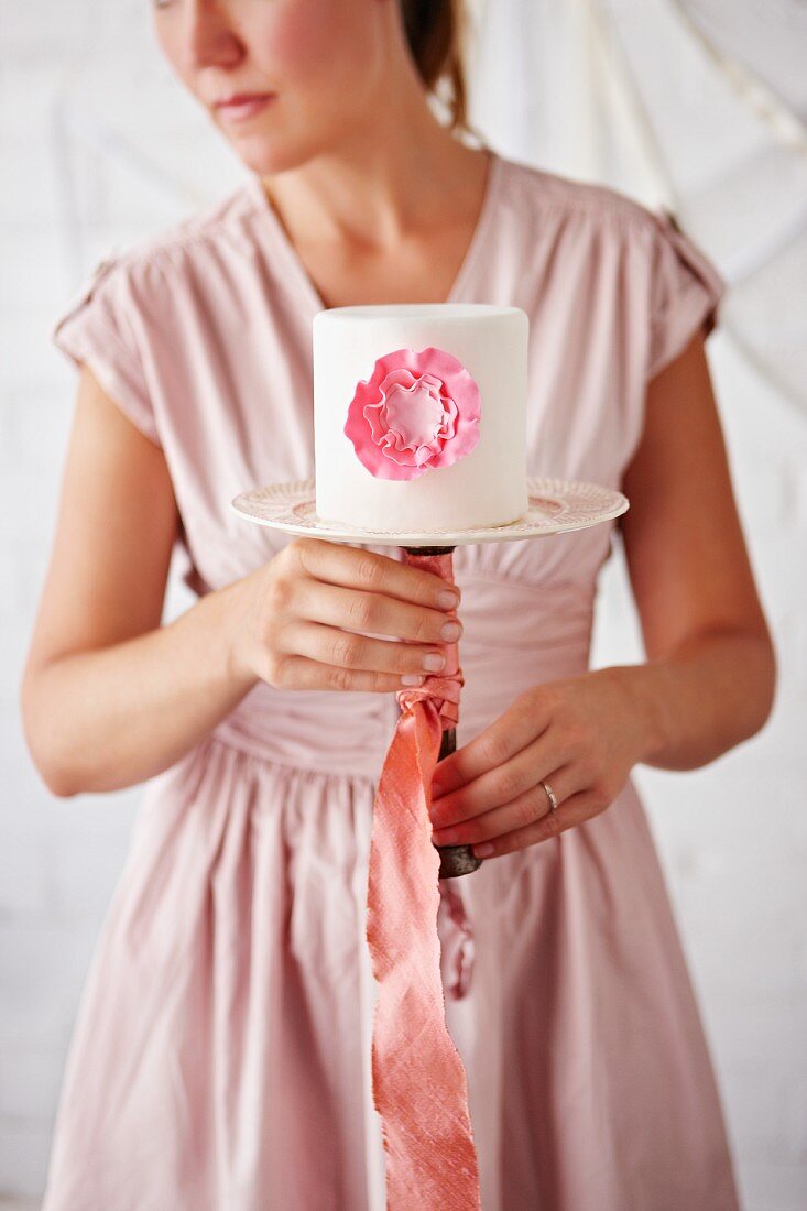 Frau hält eine weiße Torte mit rosa Verzierung auf einem Tortenständer