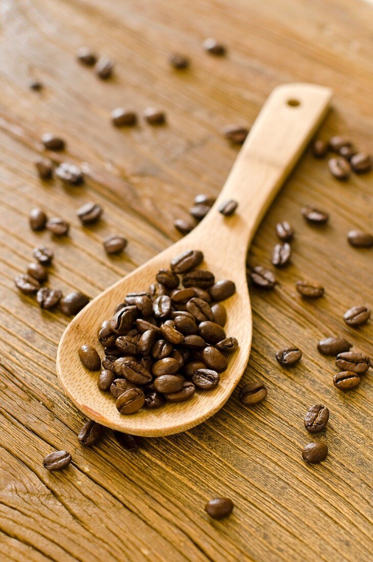 Geröstete Kaffeebohnen auf Holzlöffel und Holzuntergrund