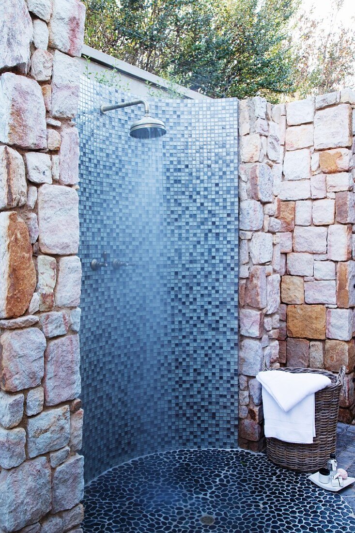 Outdoor shower with blue, mosaic tiles built into a natural stone wall