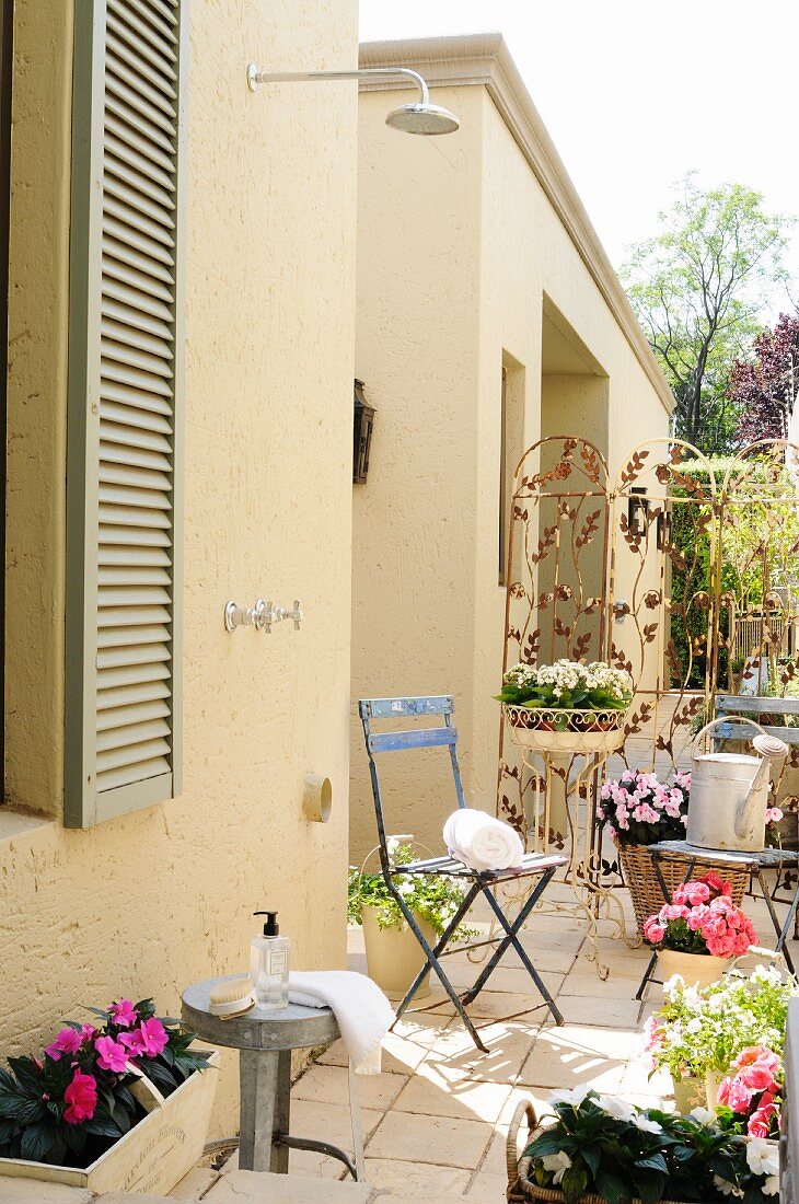 Romantic ambiance: outdoor shower mounted on an exterior house wall on a terrace decorated with plant pots and accessories