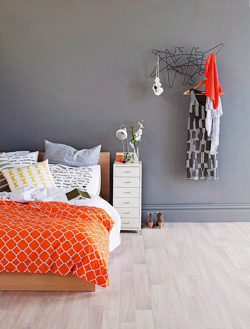 Doppelbett mit moderner, farbiger Bettwäsche neben Garderobe mit aufgehängtem Kleid an grauer Wand
