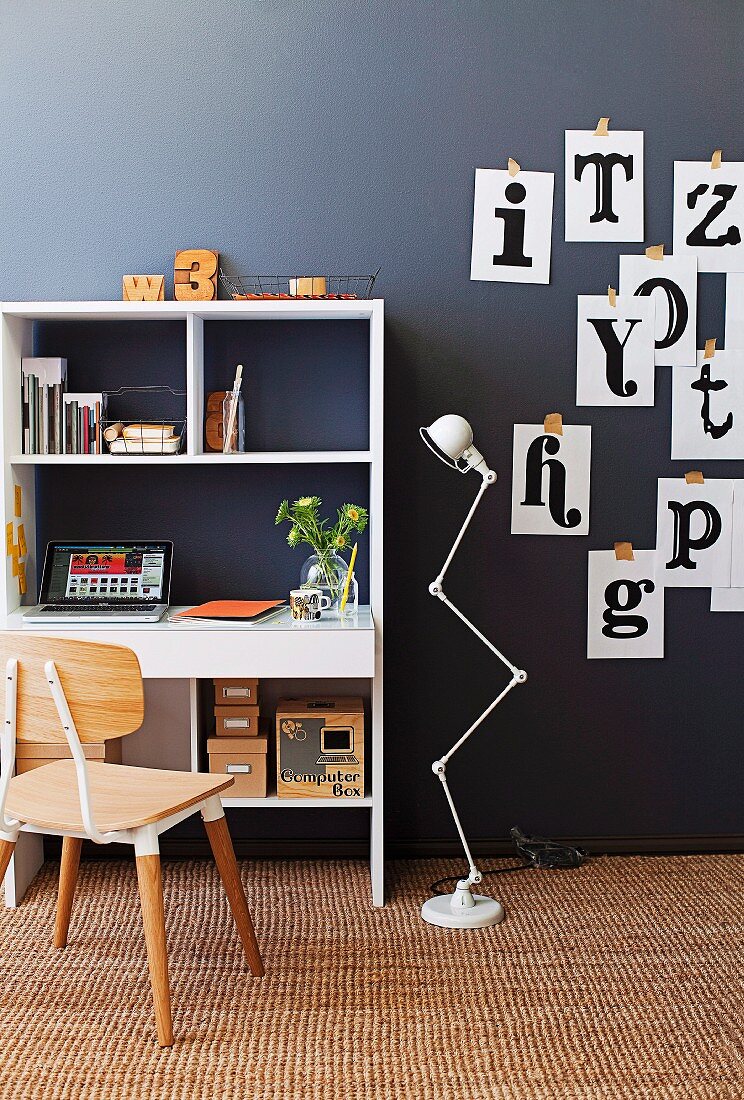 Fifties-style wooden chair in front of shelves with integrated desk and retro standard lamp against black wall decorated with images of letters