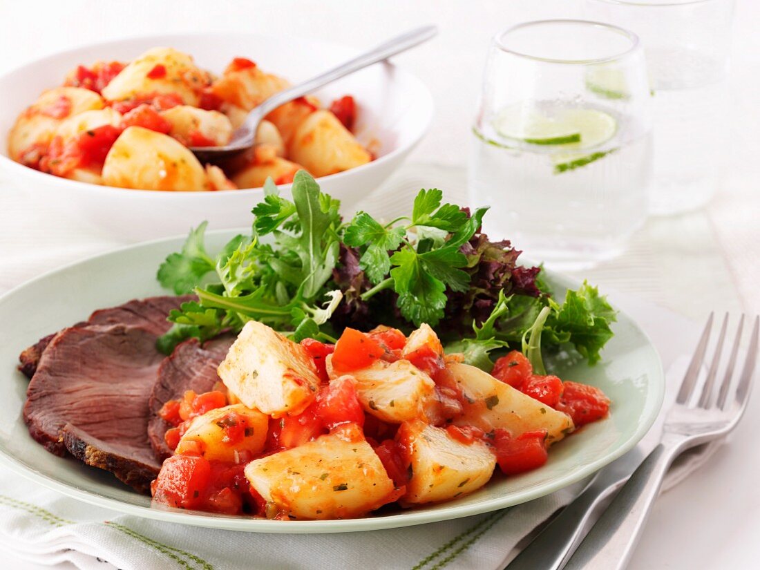 Beef with a side of tomatoes and potatoes and a mixed leaf salad