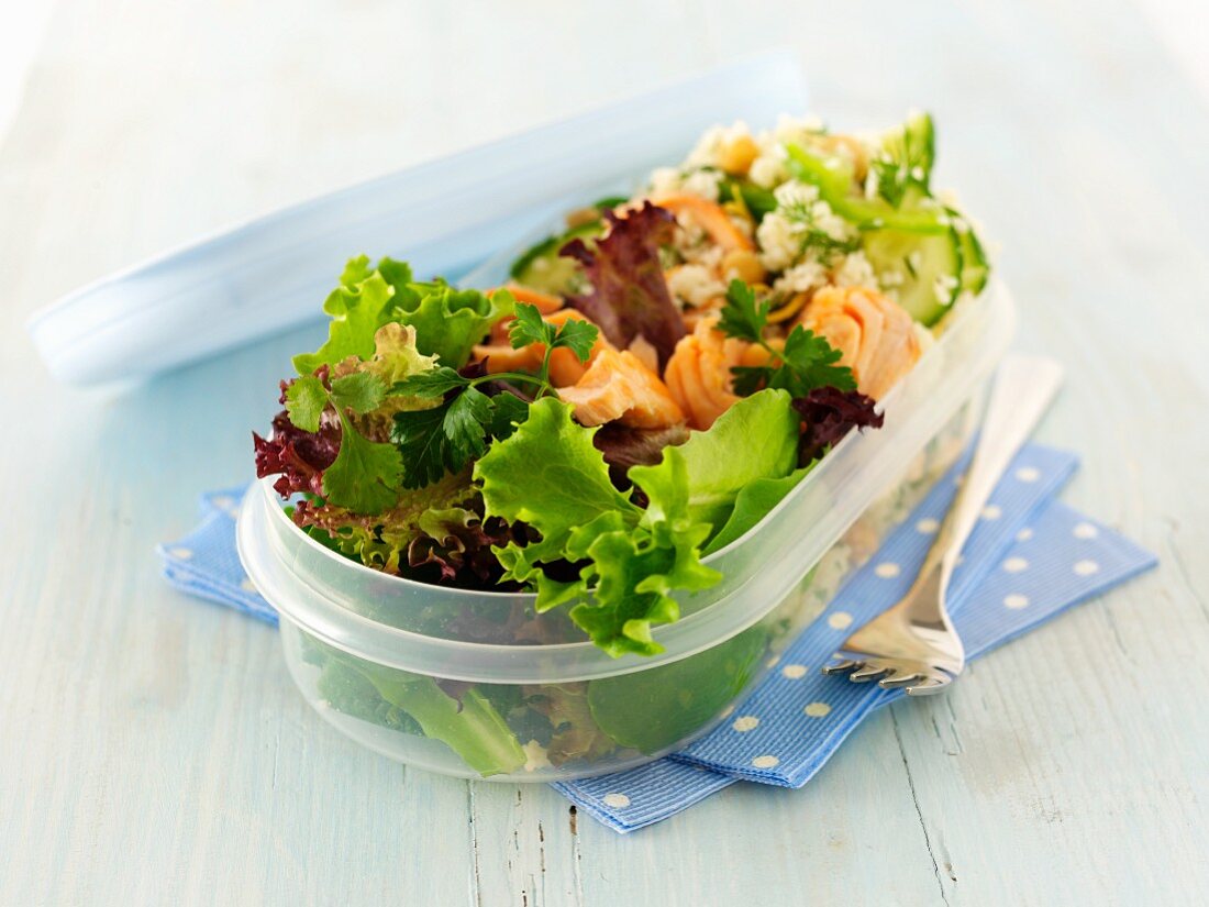 Lachs-Couscous-Salat und Blattsalat in einer ovalen Tupper