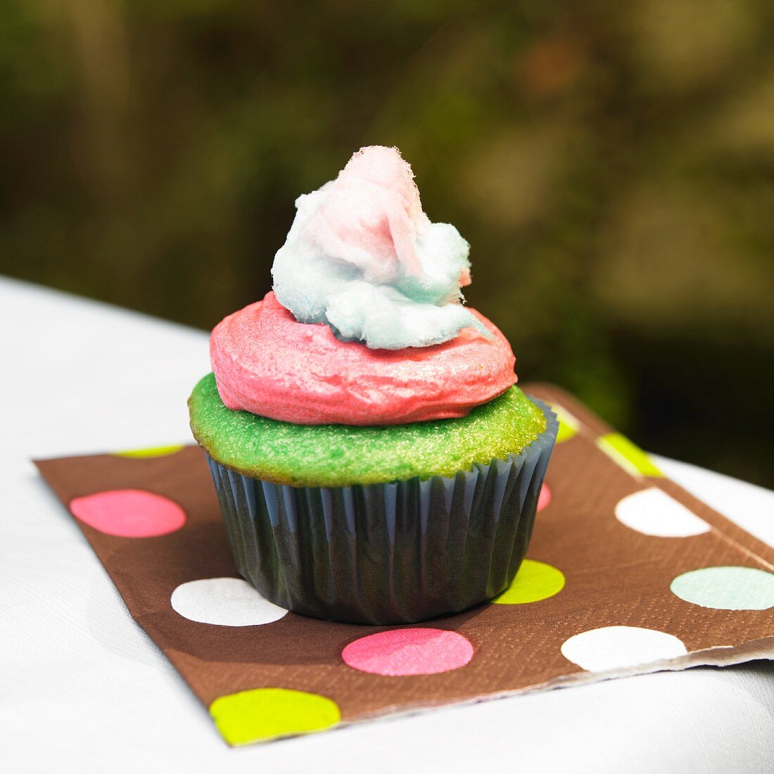 Ein grüner Cupcake mit rosa Frosting & Zuckerwatte auf Serviette