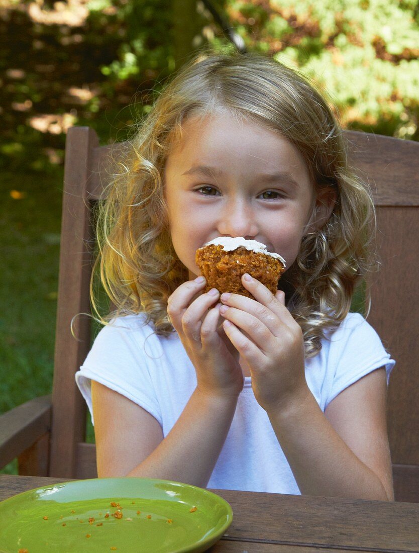 Kleines Mädchen isst Cupcake an Tisch im Freien