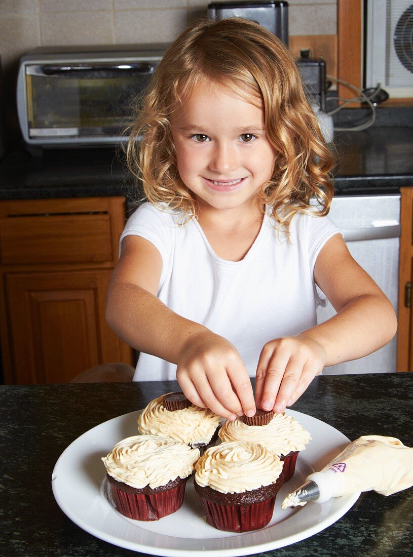 Kleines Mädchen dekoriert Cupcakes in der Küche