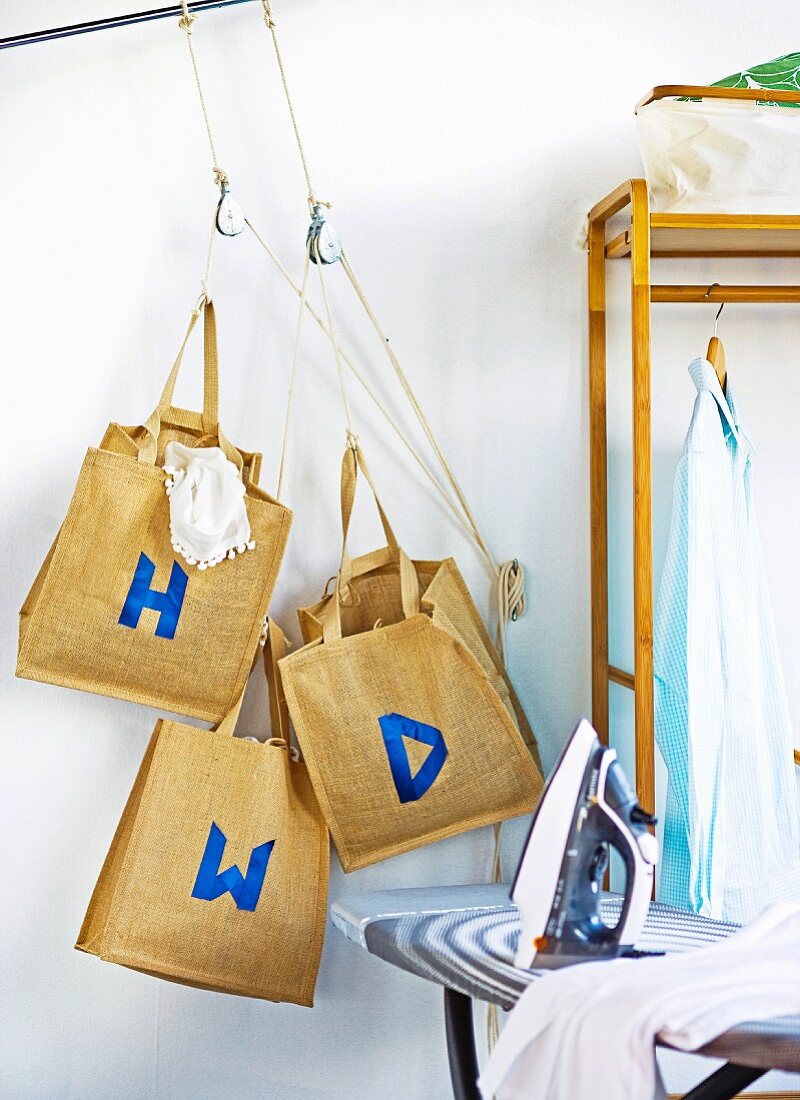 Blue letters on linen bags hanging next to clothes rack and iron on ironing board