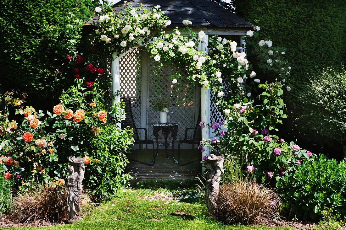 Offener Pavillon mit Kletterrosen berankt in blühendem Garten