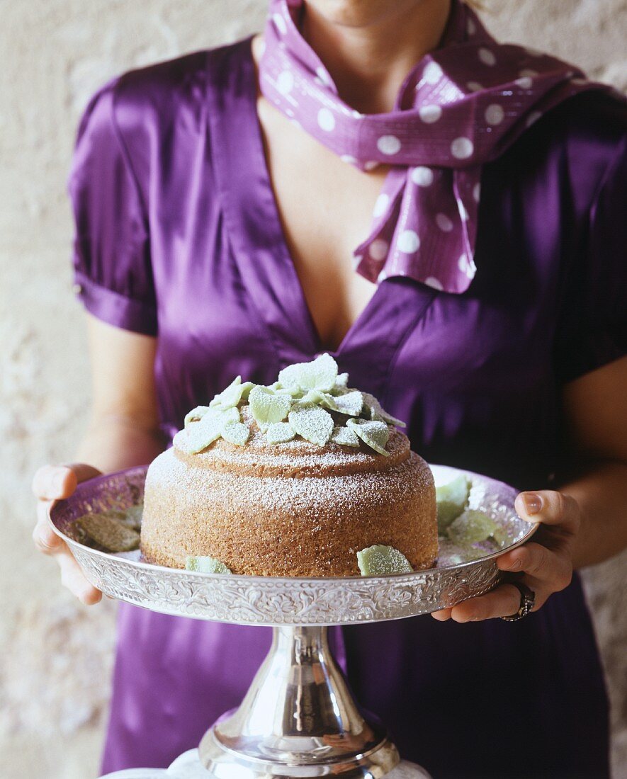 A woman in a purple dress holding a cake on a silver stand