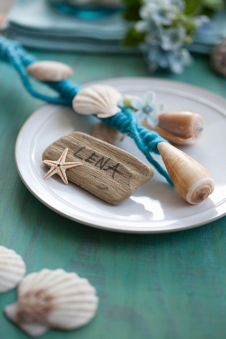 Rod decorated with felt ribbon and seashells on plate with name tag