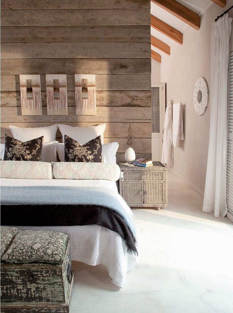 Drapierte Kissen auf Doppelbett an rustikaler Bretterwand als Raumteiler und raumhoher Durchgang ins anliegende Bad