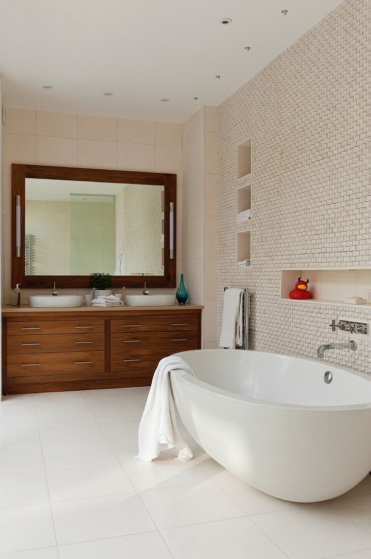 Spacious bathroom with spotlights in ceiling above oval bathtub, washstand area with exotic wood base cabinet and mirror with lamps on either side